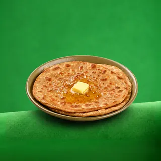 A plate of golden-brown parathas topped with a melting cube of butter, set against a solid green background.