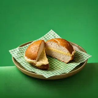 A bun cut in half with butter spread inside, served on a checkered paper liner on a plate against a green background.