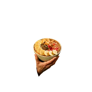A hand holding a ceramic bowl filled with oatmeal topped with sliced bananas, pomegranate seeds, pumpkin seeds, and peanut butter, isolated against a grey background.