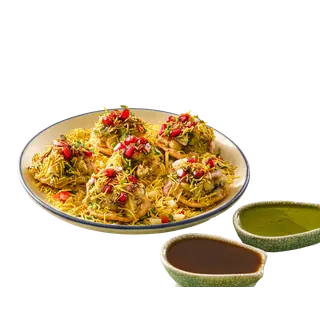 A plate of sev puri garnished with sev and pomegranate seeds, served with green and brown chutneys on a solid grey background.