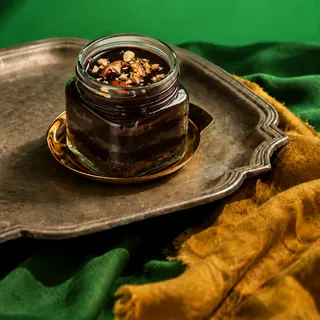 A chocolate jar cake topped with chopped nuts is presented on a golden saucer and a vintage metal tray against a green background.