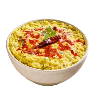 A bowl of yellow khichdi topped with red chili oil, a dried red chili, and a coriander leaf, isolated on a grey background.