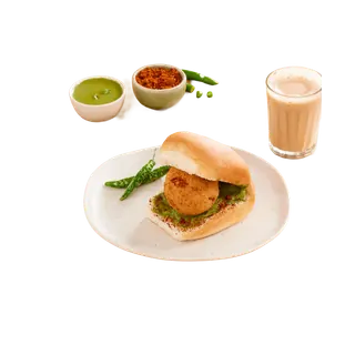 A vada pav served on a plate with green chilies, accompanied by bowls of green chutney, dry garlic chutney, and a glass of tea, isolated on a grey background.